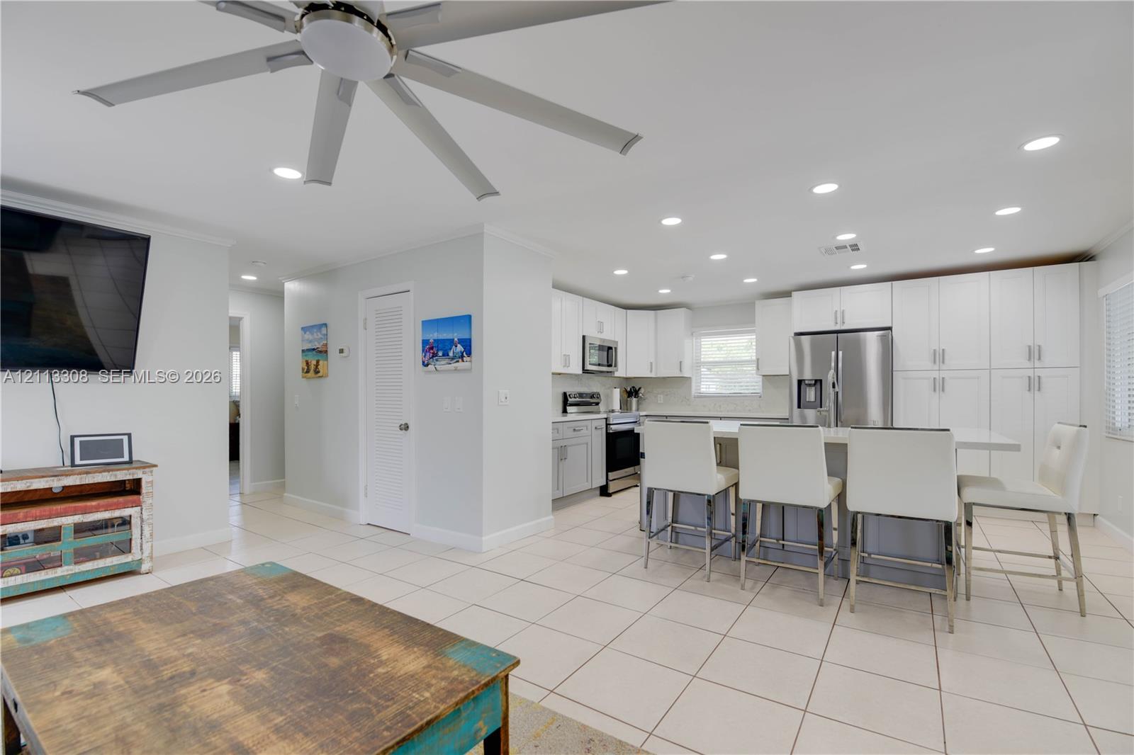 Open-concept kitchen featuring white shaker-style cabinetry, stainless steel appliances, quartz-surface breakfast bar, recessed lighting, and large-format tile flooring Open-concept kitchen featuring white shaker-style cabinetry, stainless steel appliances, quartz-surface breakfast bar, recessed lighting, and large-format tile flooring