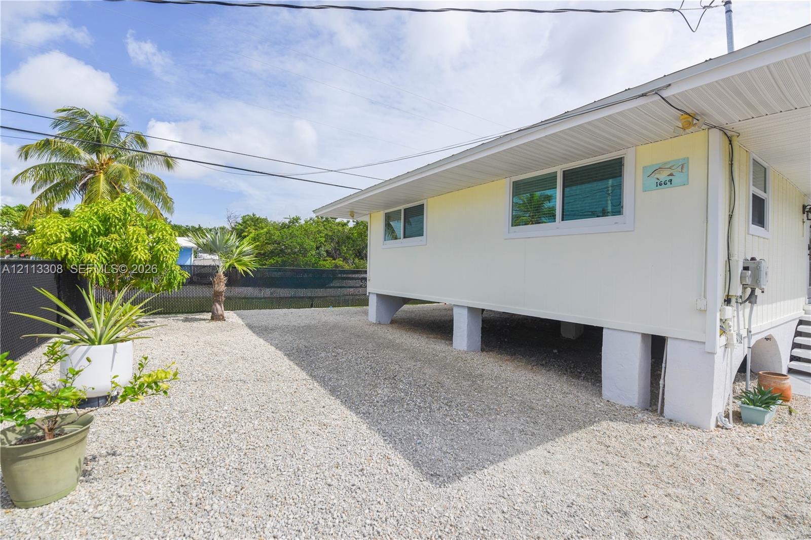 Elevated structure featuring light-colored horizontal siding, dual-pane horizontal sliding windows, and a gravel ground surface