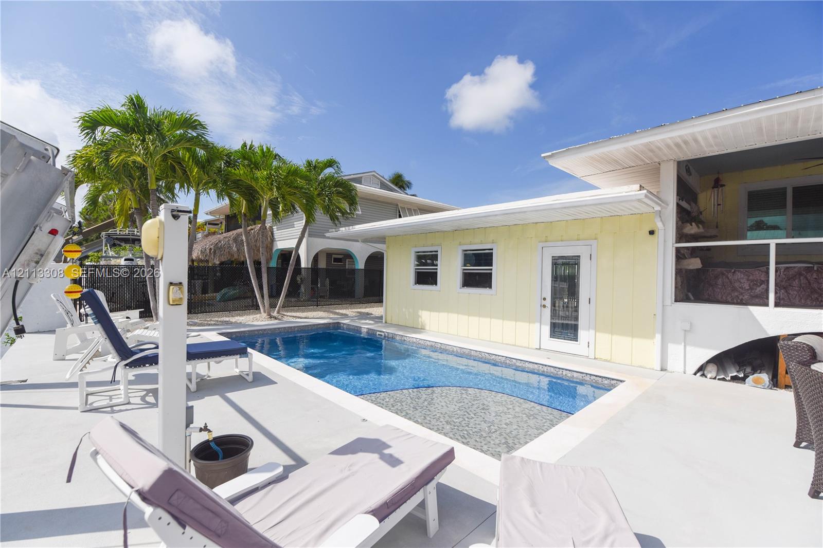 In-ground swimming pool with tiled interior, expansive concrete deck, yellow siding exterior, and palm trees