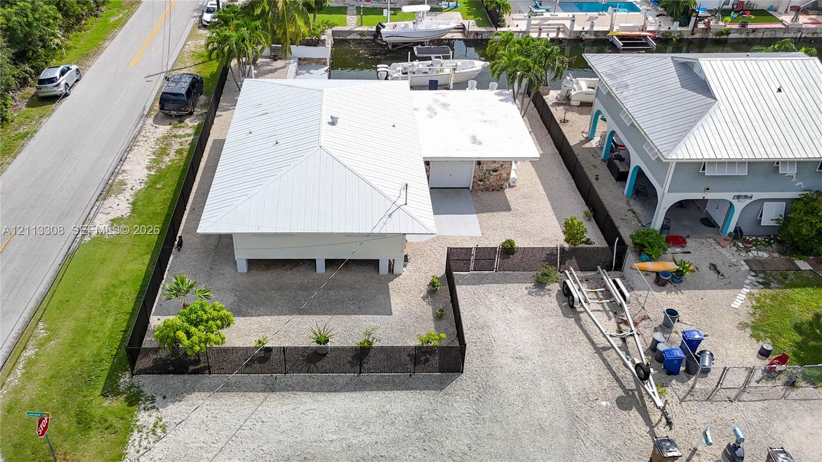 Aerial view of a waterfront property featuring a metal roof, elevated structure, stone masonry detailing, and perimeter fencing