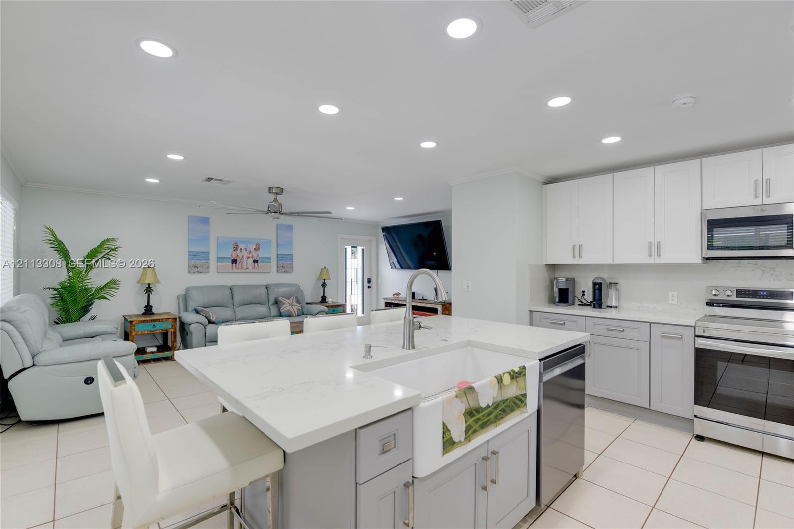 Kitchen featuring a central island with a farmhouse-style apron sink, quartz countertops, white shaker-style cabinetry, stainless steel appliances, and tile flooring