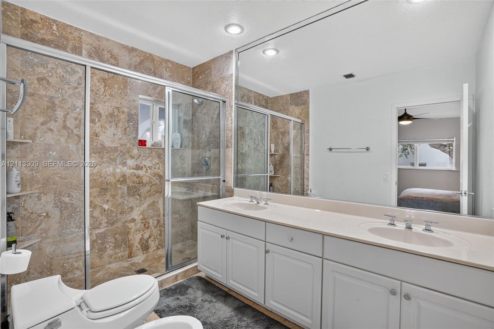 Dual-sink vanity with a solid-surface countertop, floor-to-ceiling framed mirror, and a walk-in shower featuring tile surrounds and a glass enclosure
