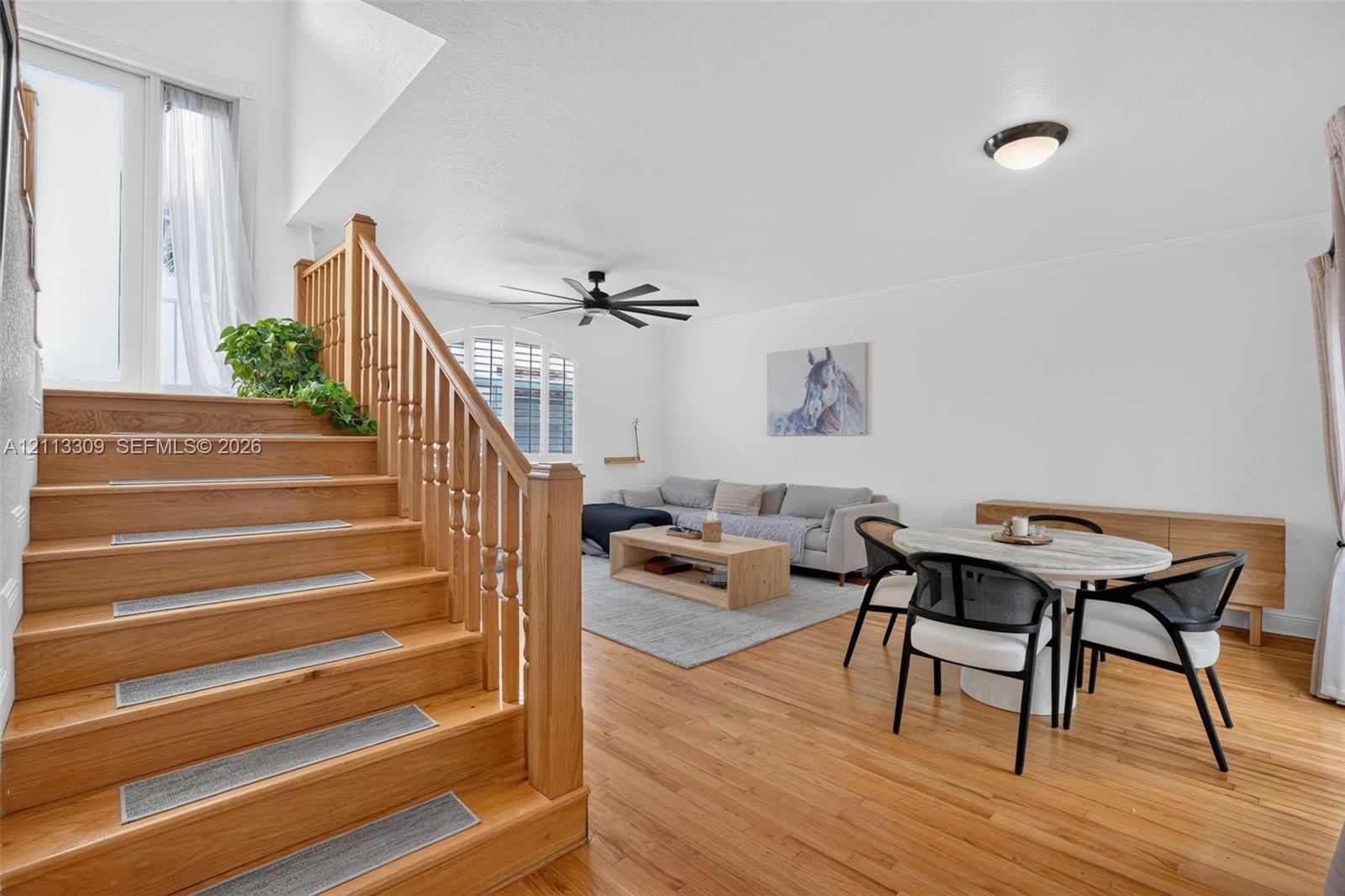 Wood-finish flooring, staircase with a wood balustrade and handrail, vaulted ceiling, and an arched window