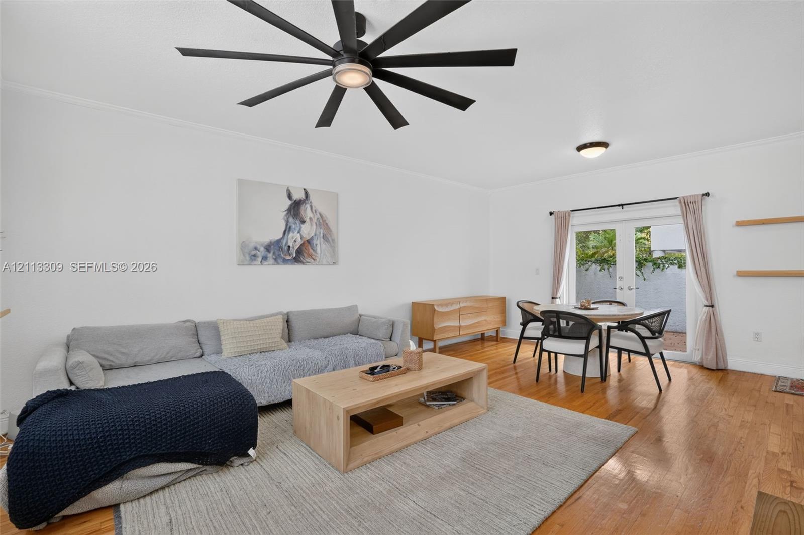 Interior space featuring wood-finish flooring, a contemporary multi-blade ceiling fan, glass-paned double doors, and wall-mounted floating shelves
