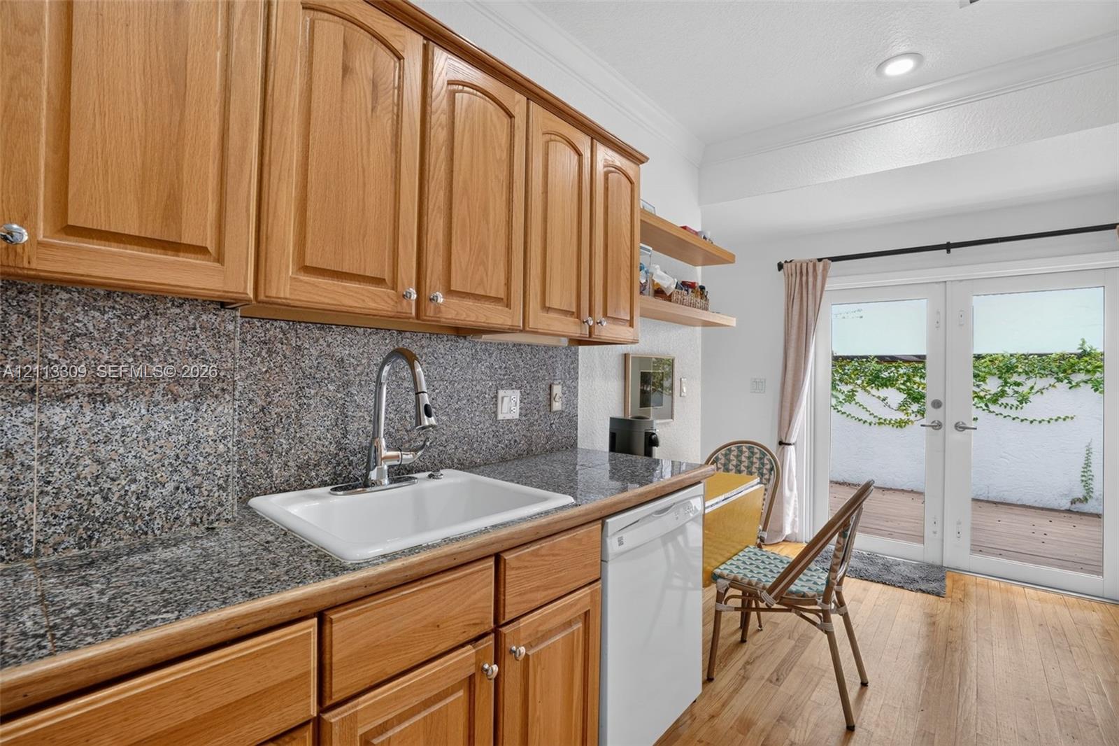 Kitchen featuring wood cabinetry, stone-surface countertop, integrated white sink with pull-down faucet, recessed ceiling lighting, and double glass-panel doors
