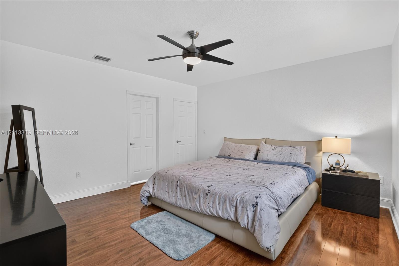 Neutral wall finish, wood-finish flooring, two paneled interior doors, and a ceiling-mounted fan with integrated lighting