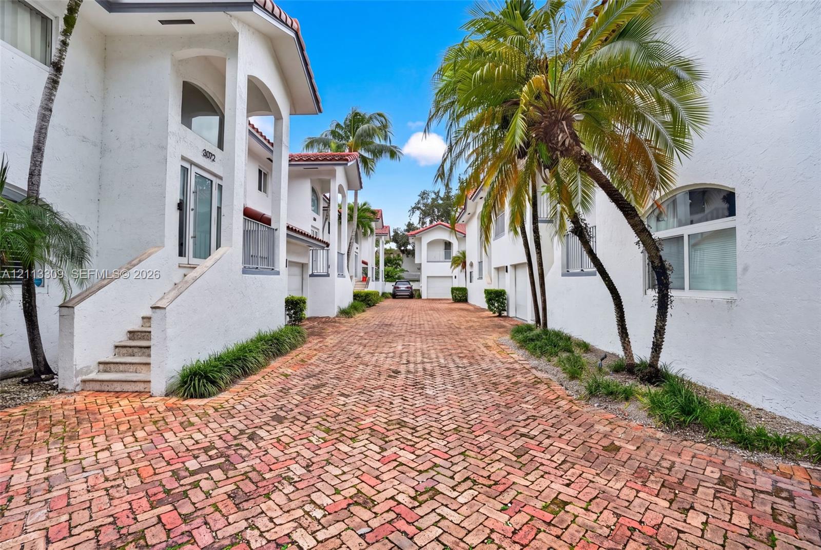 Stucco exterior featuring arched architectural detailing, a herringbone-patterned brick paver motor court, and mature palm landscaping