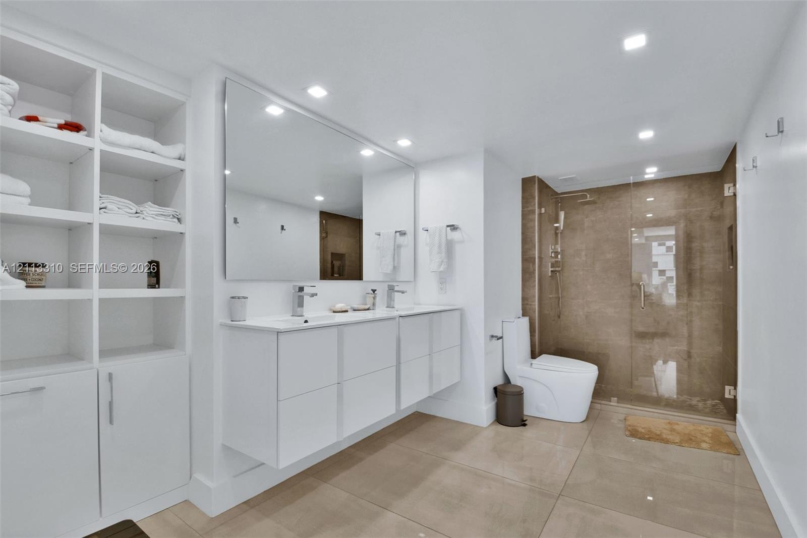 Bathroom featuring a floating double vanity with rectangular sinks, a floor-to-ceiling white built-in storage cabinet, large-format tile flooring, and a walk-in shower with a glass enclosure and tiled walls