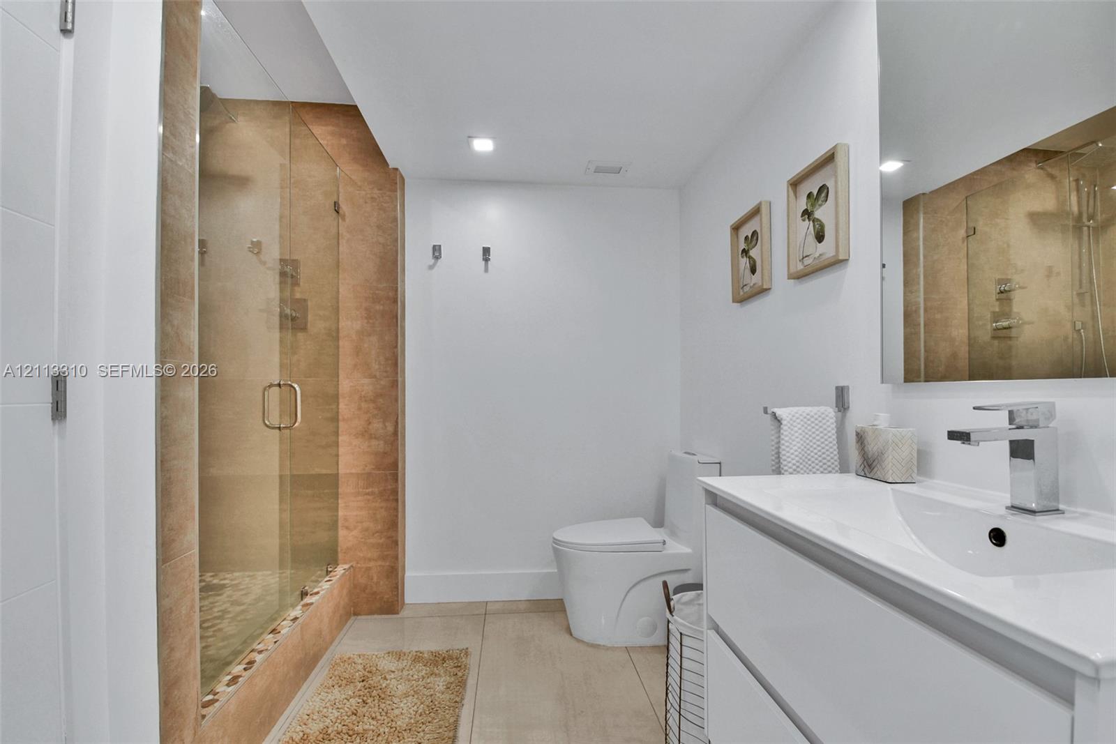 Bathroom featuring a glass-enclosed walk-in shower with textured wall tile, a white vanity with an integrated basin, a polished chrome faucet, and a wall-mounted mirror