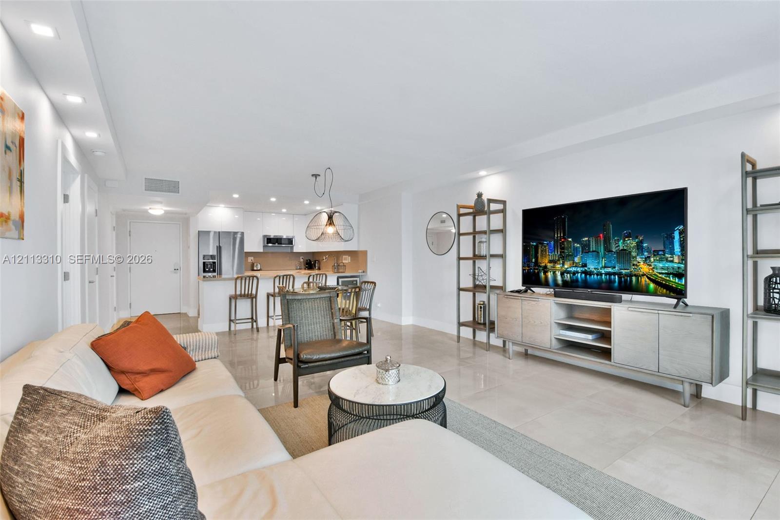 Open-concept living space featuring high-gloss white cabinetry, polished tile flooring, recessed ceiling lighting, and a breakfast bar
