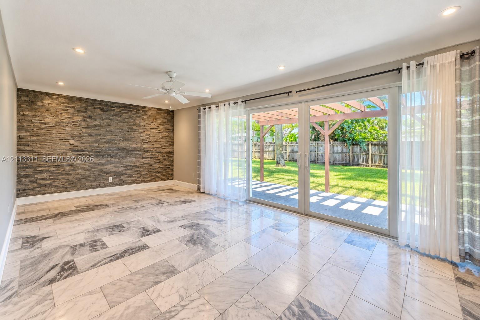 Stone veneer accent wall, large-format tile flooring, recessed lighting, and sliding glass doors opening to a covered patio with a wooden pergola