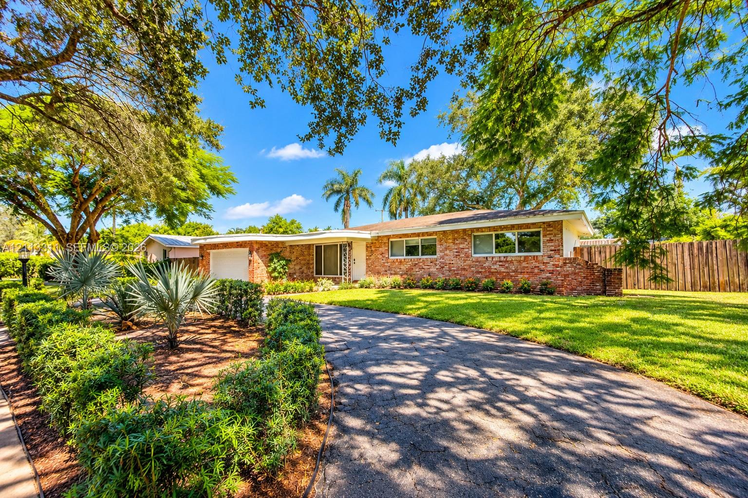 Ranch-style exterior featuring a multi-tonal brick faade, an attached single-car garage, an expansive manicured lawn, established landscaping, and a curved driveway