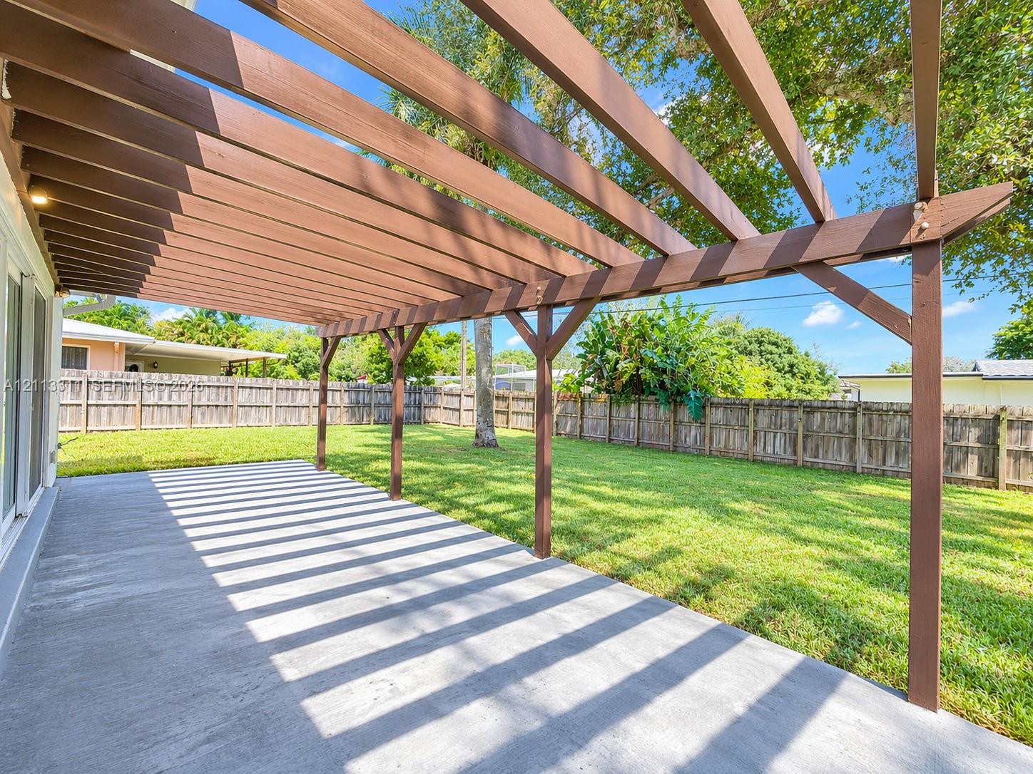 Outdoor patio featuring a stained wood pergola, concrete flooring, and a fenced backyard
