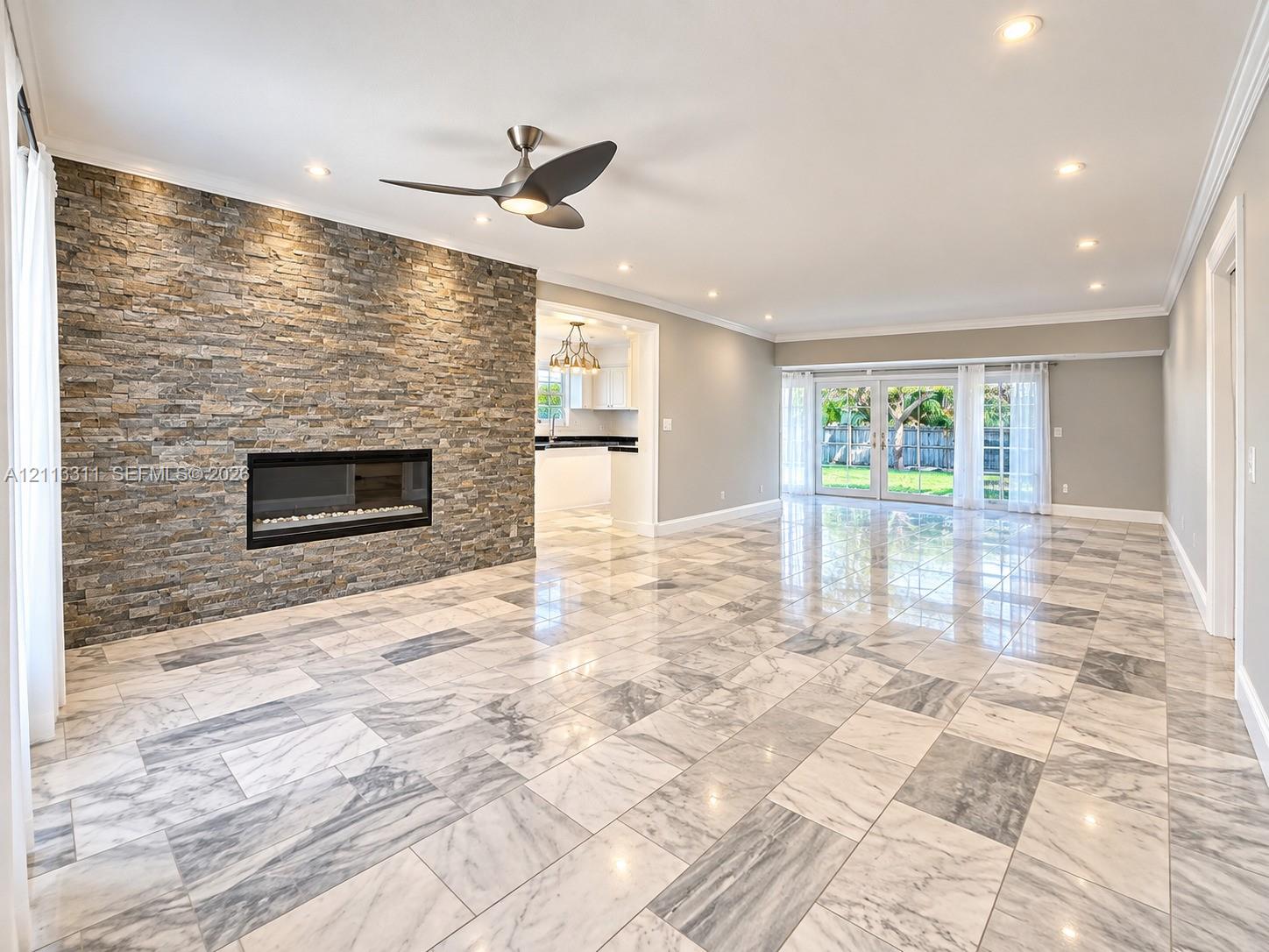 Open-concept space featuring a floor-to-ceiling stacked-stone fireplace, polished stone flooring, recessed lighting, and glass-paneled double doors