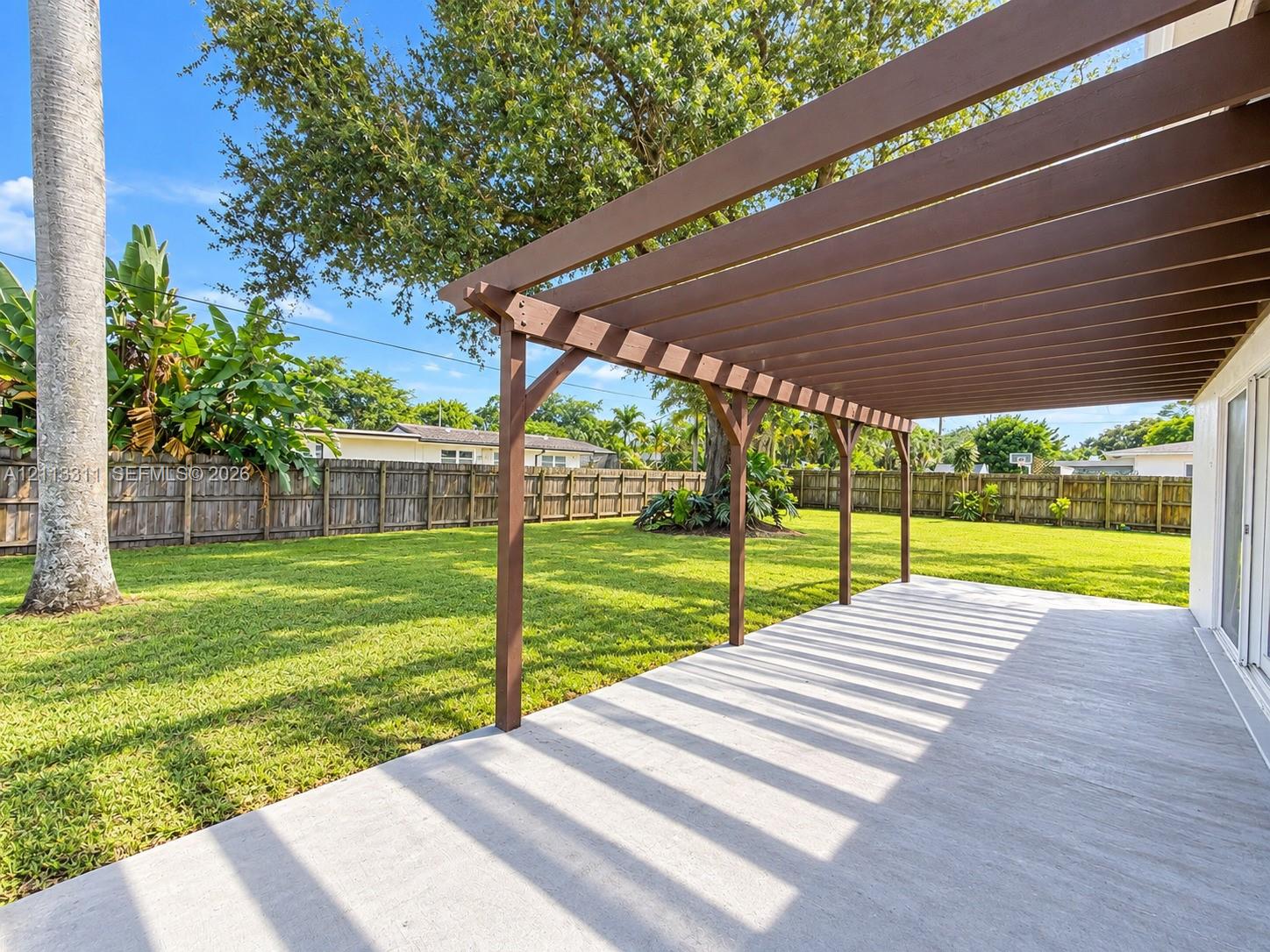 Concrete patio featuring a wooden pergola, expansive fenced-in backyard, and mature landscaping