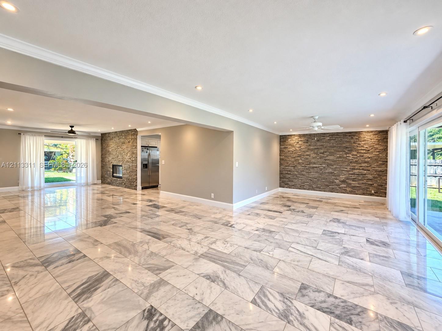 Spacious living area featuring polished stone flooring, stacked stone accent walls, recessed lighting, and multiple sliding glass doors