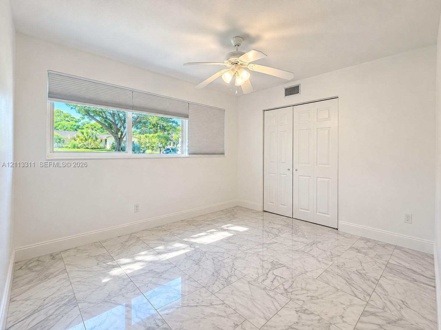 Polished stone-finish tile flooring, ceiling fan with integrated lighting, dual-panel closet doors, and a wide horizontal window with installed blinds