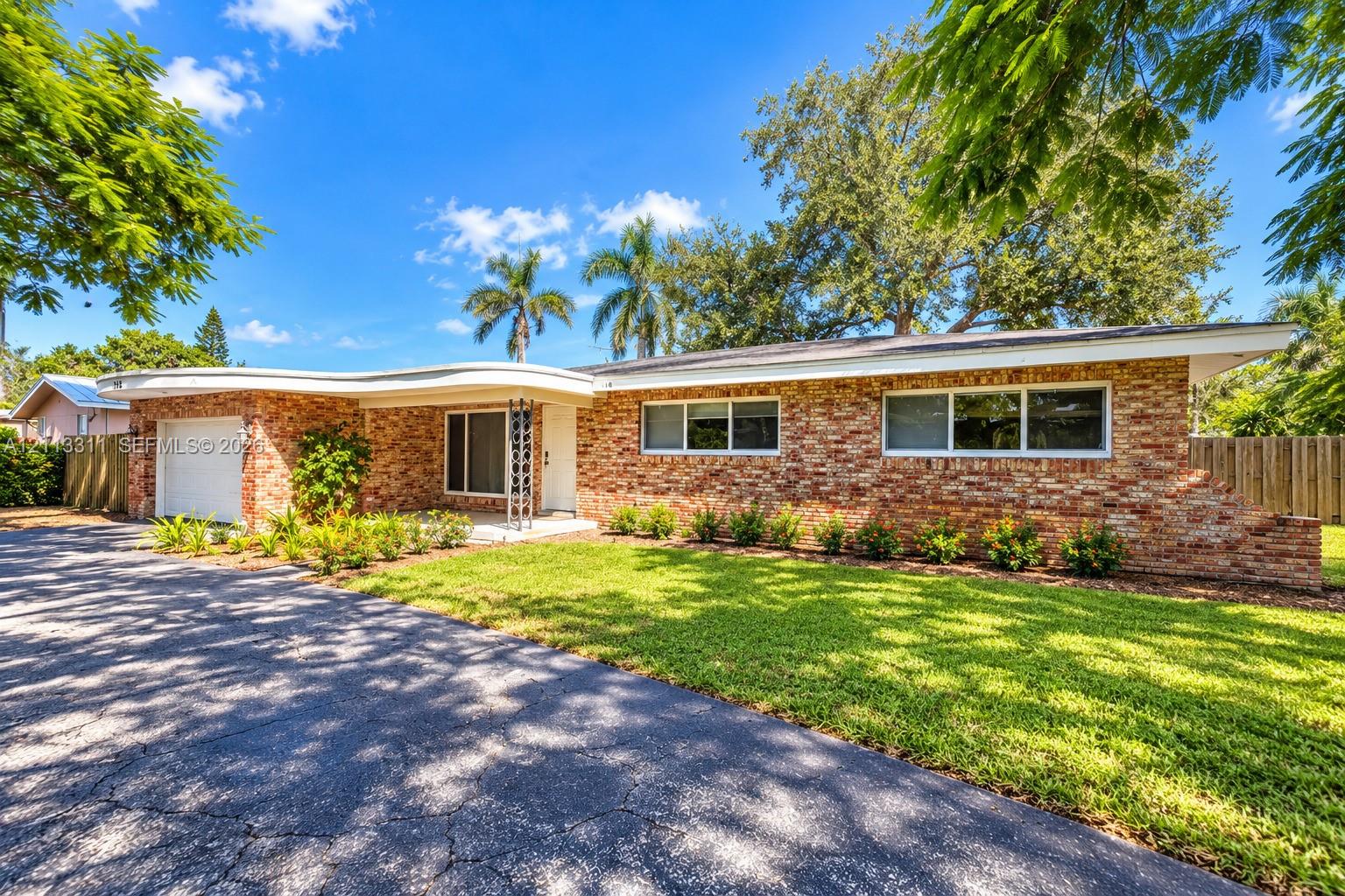 Single-story brick exterior featuring a distinctive curved roofline, an attached garage, a paved driveway, and mature landscaping