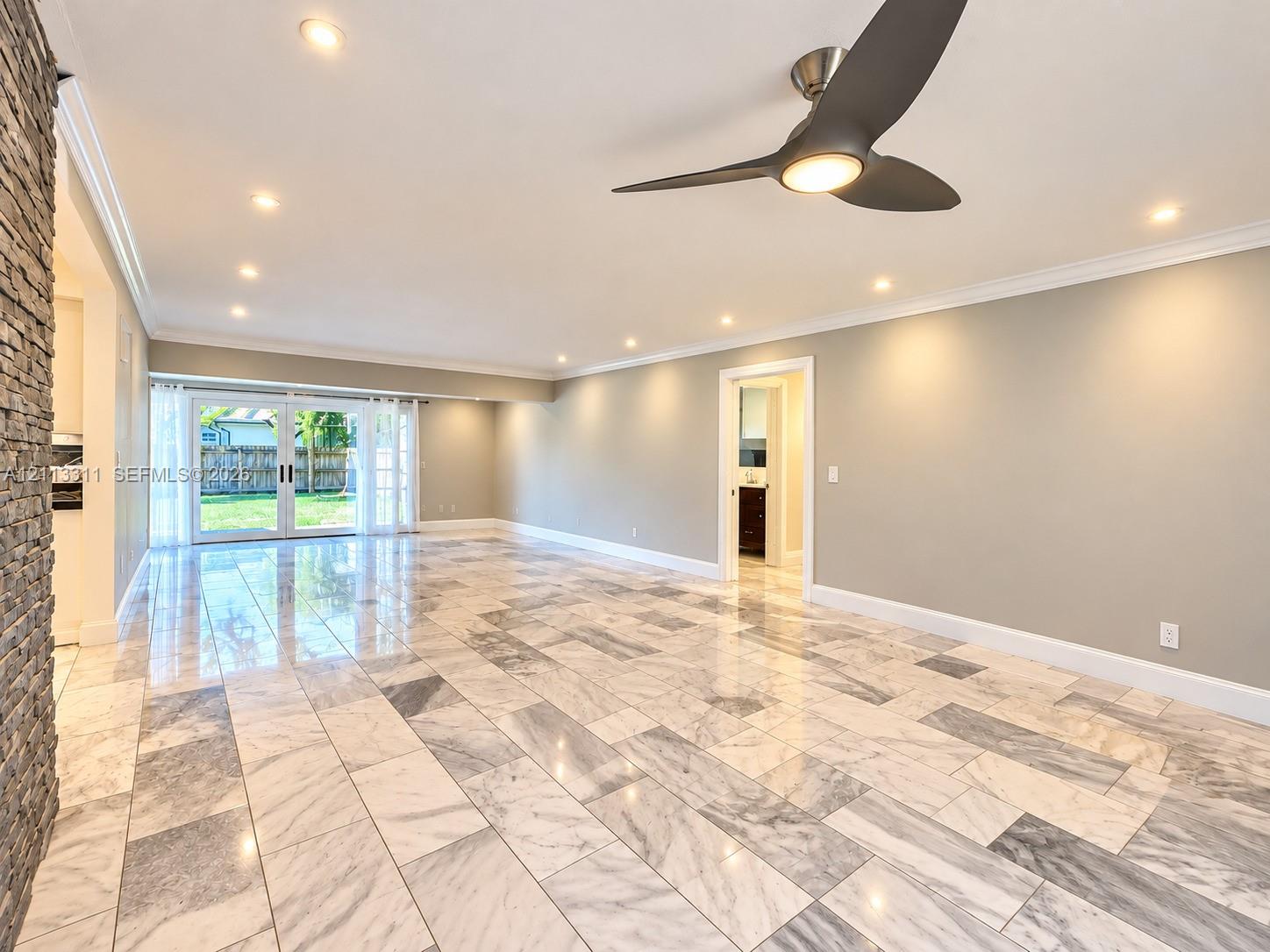 Polished tile flooring, crown molding, stone-accented pillar, three-blade ceiling fan with integrated lighting, and glass-paneled double doors