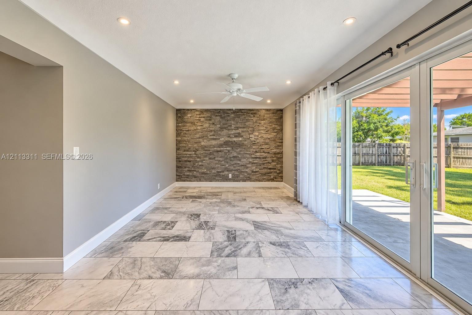 Interior space featuring large-format tile flooring, a stone-veneer accent wall, recessed lighting, and sliding glass doors opening to a covered patio