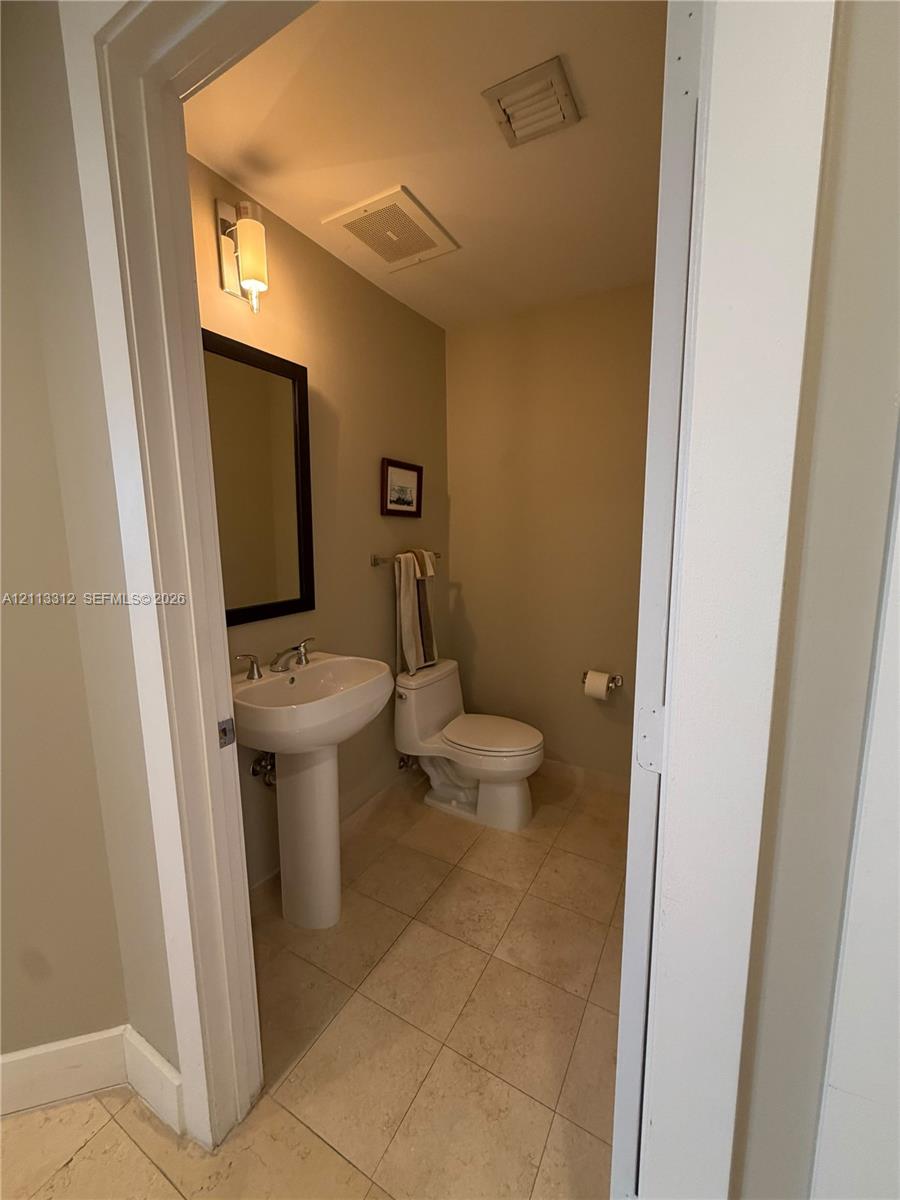 Powder room featuring a porcelain pedestal sink, stone-finish floor tiling, wall-mounted vanity lighting, and a framed mirror Powder room featuring a porcelain pedestal sink, stone-finish floor tiling, wall-mounted vanity lighting, and a framed mirror