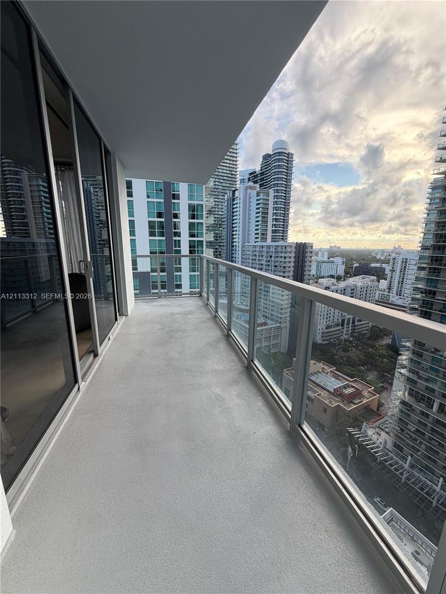Covered outdoor balcony featuring a concrete floor, glass railings, and expansive cityscape horizons Covered outdoor balcony featuring a concrete floor, glass railings, and expansive cityscape horizons