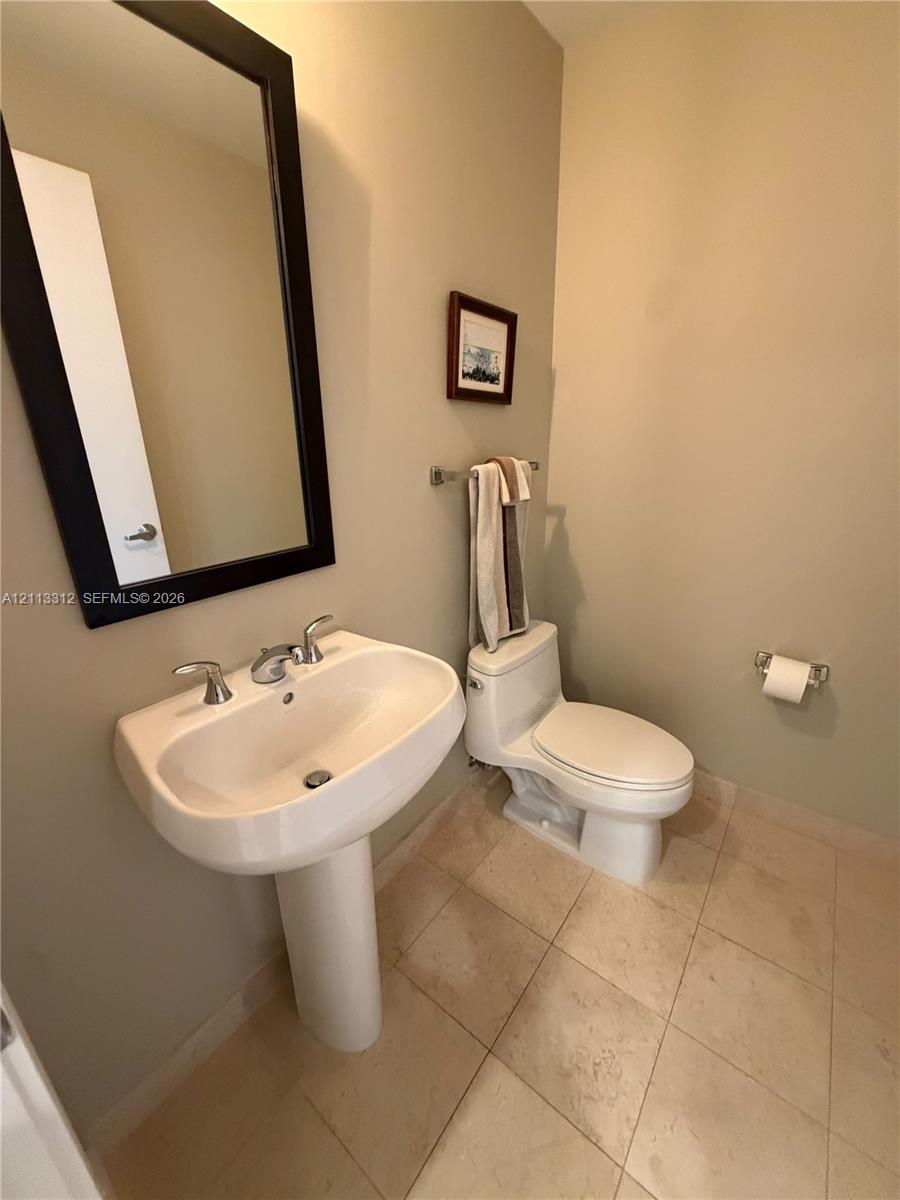 White pedestal sink with chrome faucet, neutral tile flooring, and wall-mounted mirror with a dark frame White pedestal sink with chrome faucet, neutral tile flooring, and wall-mounted mirror with a dark frame