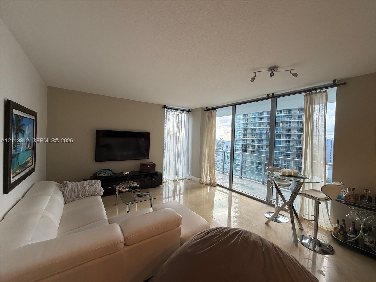 Floor-to-ceiling glass wall, polished tile flooring, integrated balcony access, and track lighting Floor-to-ceiling glass wall, polished tile flooring, integrated balcony access, and track lighting
