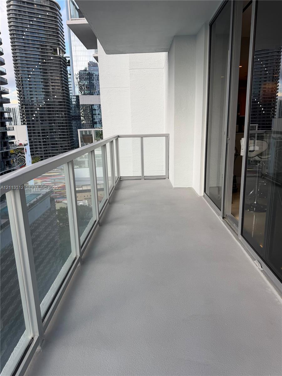 Private balcony featuring neutral concrete flooring and a glass-paneled railing with a metal frame, accessible via floor-to-ceiling sliding glass doors