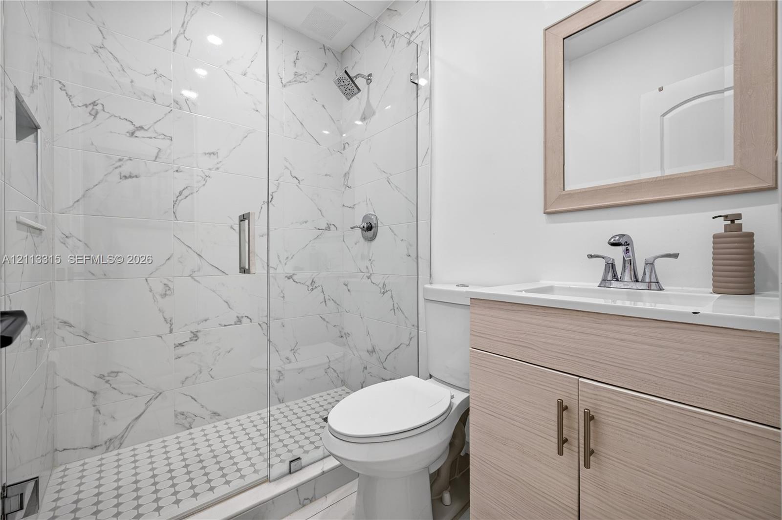 Walk-in shower featuring large-format stone-patterned tile walls, a frameless glass door, and a geometric mosaic tile floor