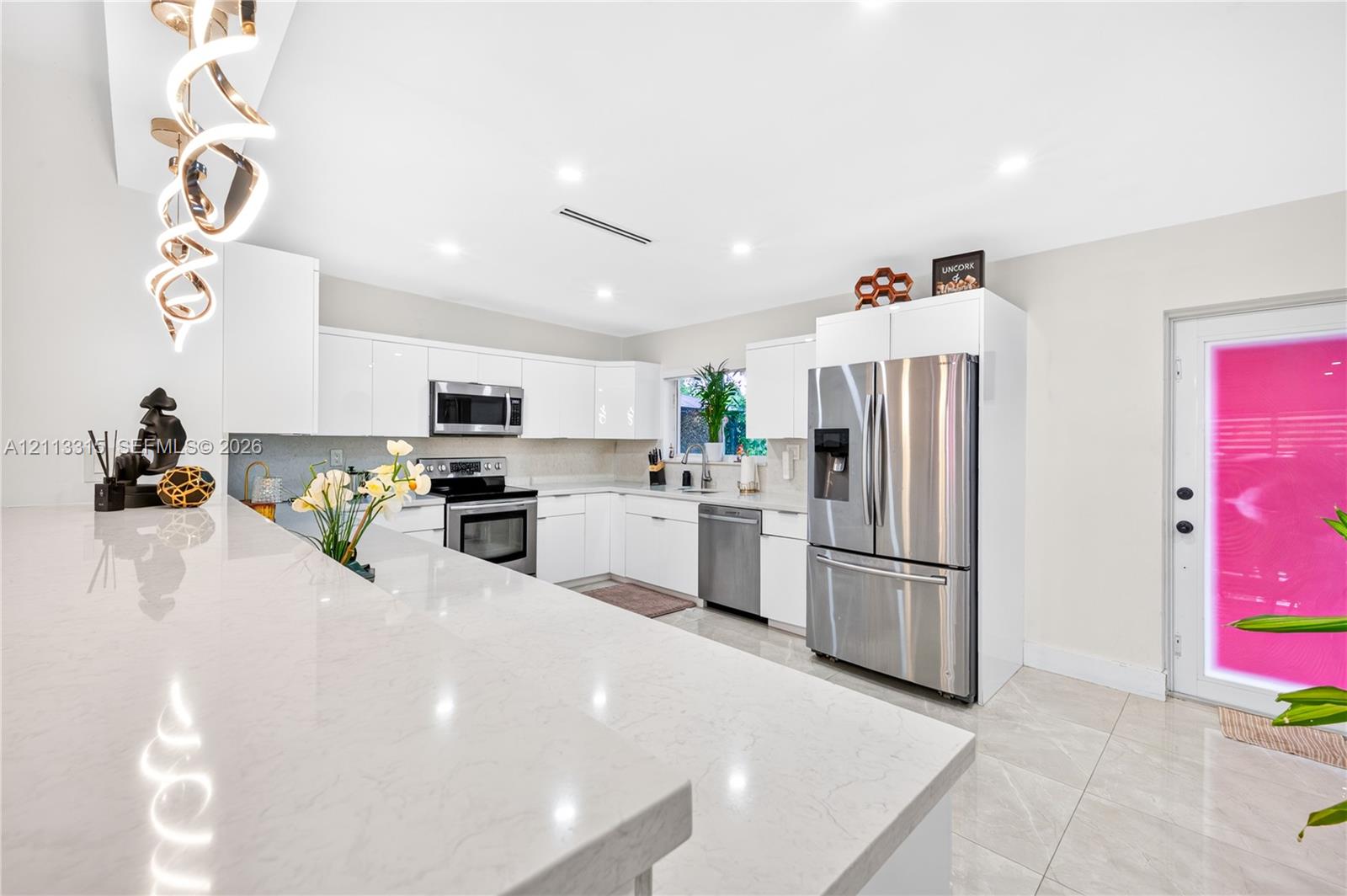 Kitchen featuring white slab-front cabinetry, quartz countertops, stainless steel appliances, large-format tile flooring, and a decorative spiral chandelier