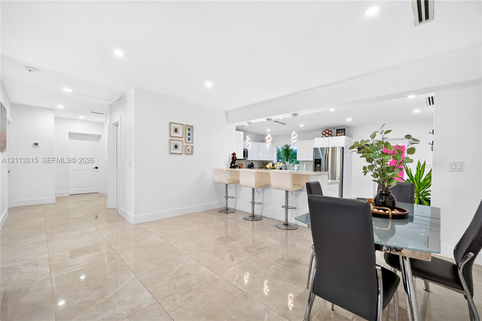 Large-format tile flooring, recessed ceiling lighting, and a breakfast bar with stone-finish countertops