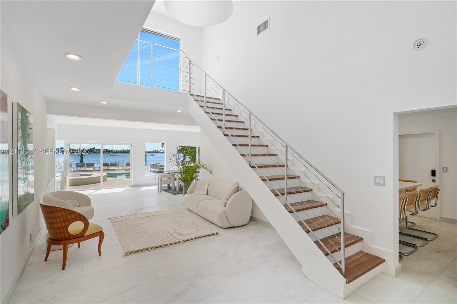 Open-concept interior featuring high ceilings, open-riser staircase with stainless steel cable railing and wood-finish treads, large-format tile flooring, and floor-to-ceiling windows Open-concept interior featuring high ceilings, open-riser staircase with stainless steel cable railing and wood-finish treads, large-format tile flooring, and floor-to-ceiling windows