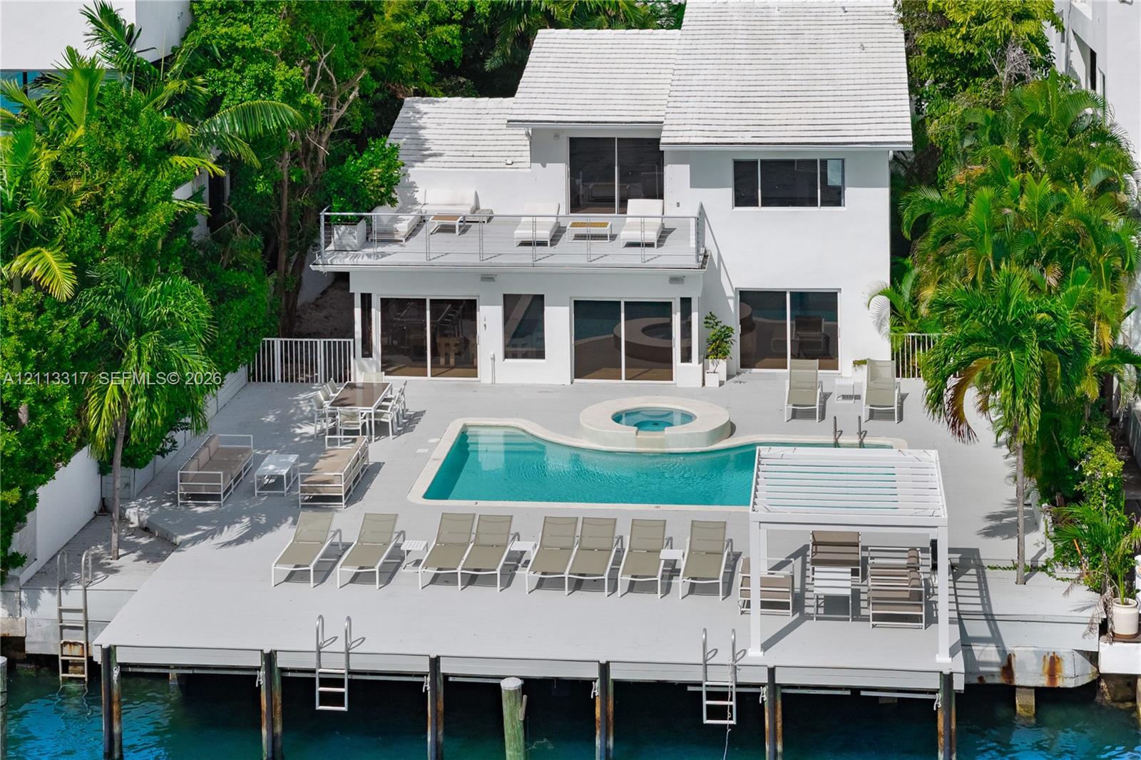 Two-story exterior with white siding and a tiled roof, featuring an expansive waterside deck, a swimming pool with an integrated spa, and a private dock