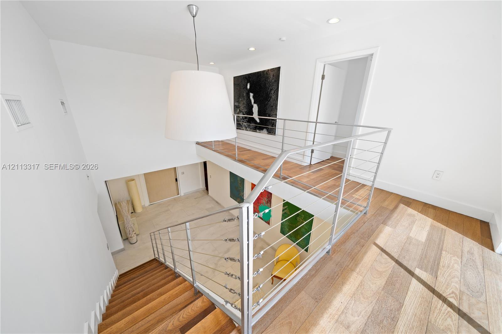 Staircase featuring wood-finish treads, metal cable railing system, recessed lighting, and a large drum pendant light Staircase featuring wood-finish treads, metal cable railing system, recessed lighting, and a large drum pendant light