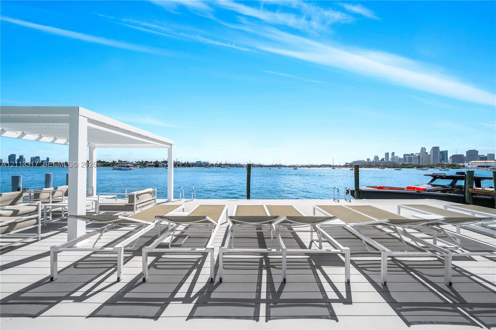 Waterfront dock featuring light-toned decking, a white pergola, and integrated marine pilings