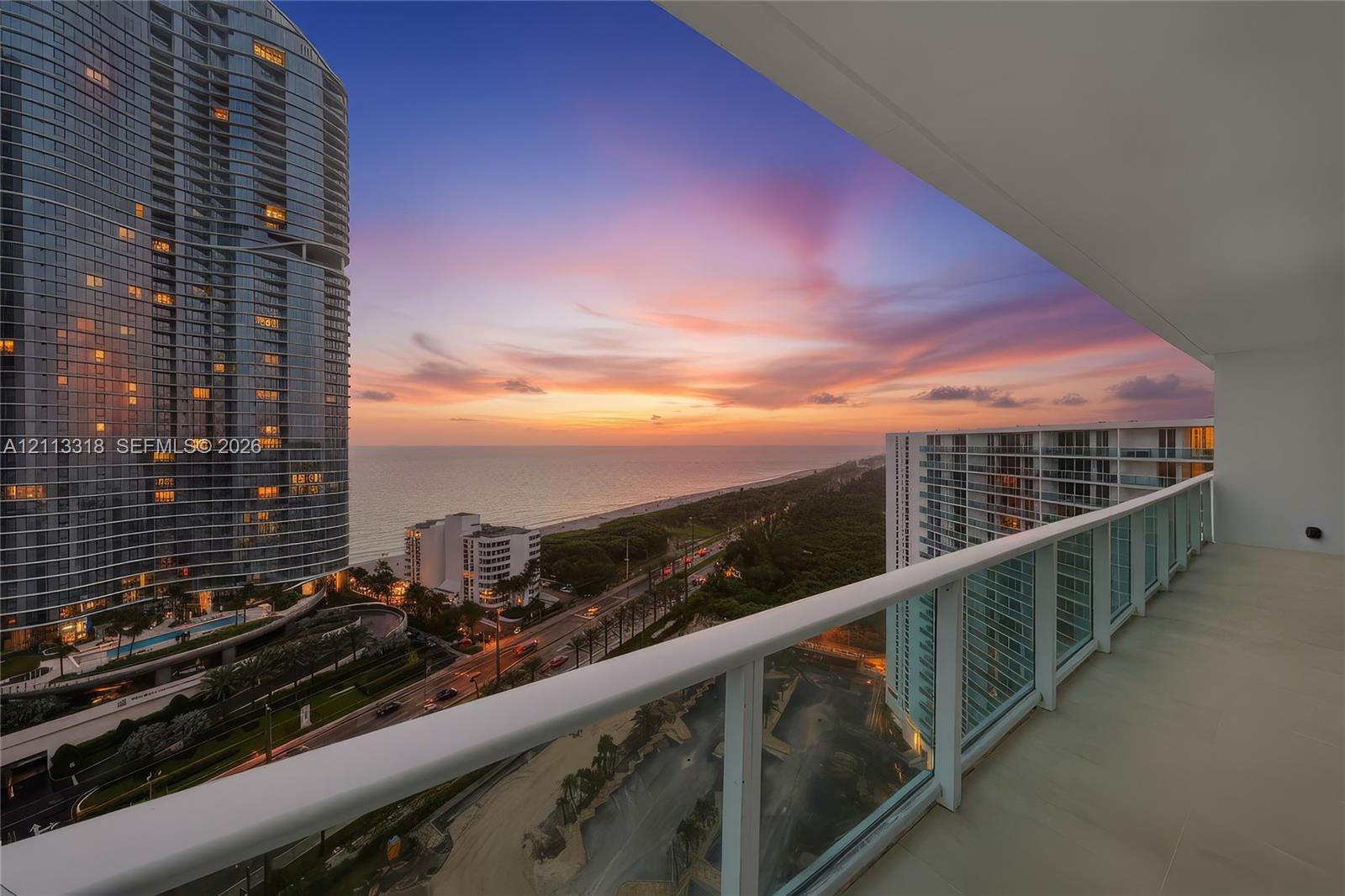 Covered balcony with a glass panel railing, tile flooring, and expansive ocean and coastal scenery