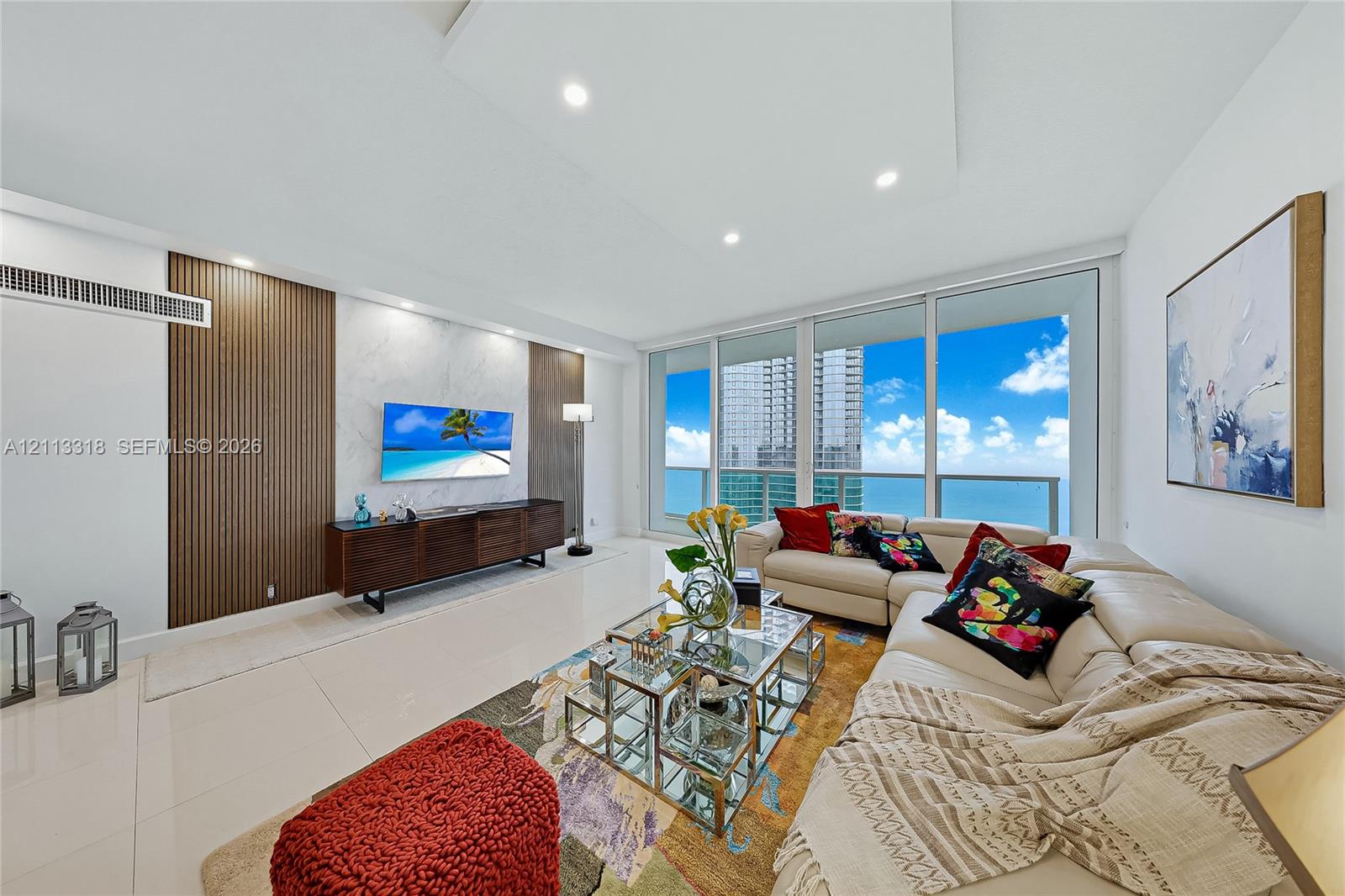 Living area featuring floor-to-ceiling windows, porcelain tile flooring, recessed ceiling lighting, and a decorative wall treatment with vertical wood-finish slats and stone-finish paneling
