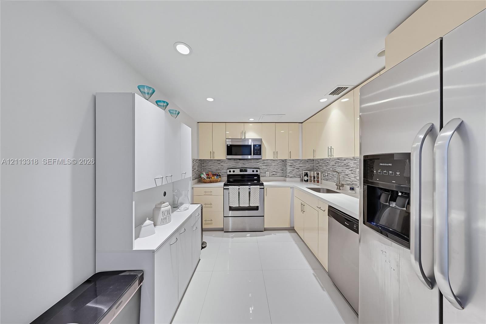 Kitchen featuring glossy cabinetry, stainless steel appliances, tile backsplash, polished stone countertops, and tile flooring