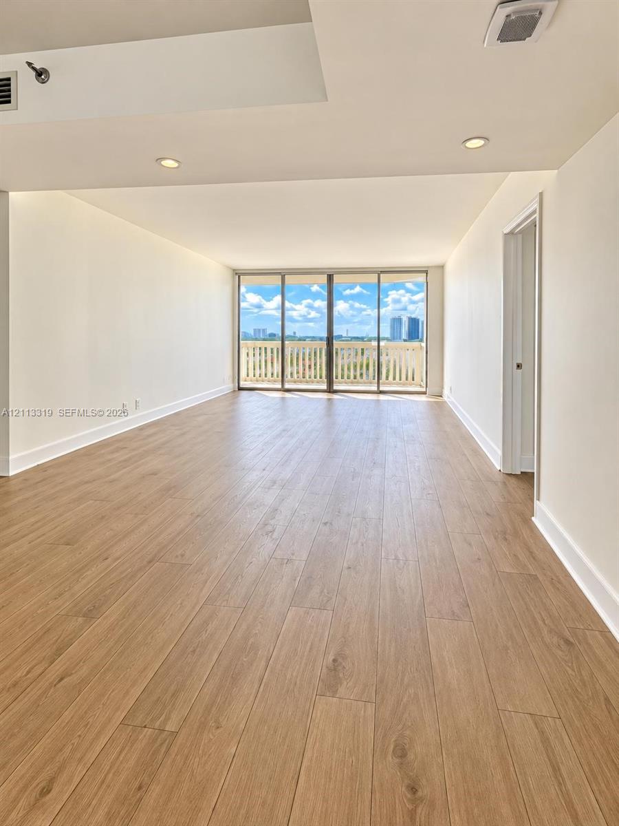Open interior featuring wood-finish flooring, recessed lighting, and floor-to-ceiling glass sliding doors opening to an exterior balcony