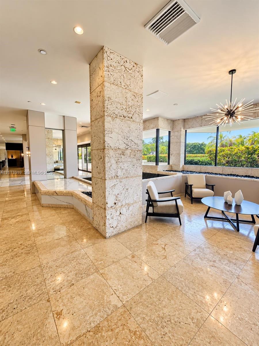 Common area featuring polished stone tile flooring, a floor-to-ceiling textured stone pillar, sunburst-style ceiling light fixture, and floor-to-ceiling windows