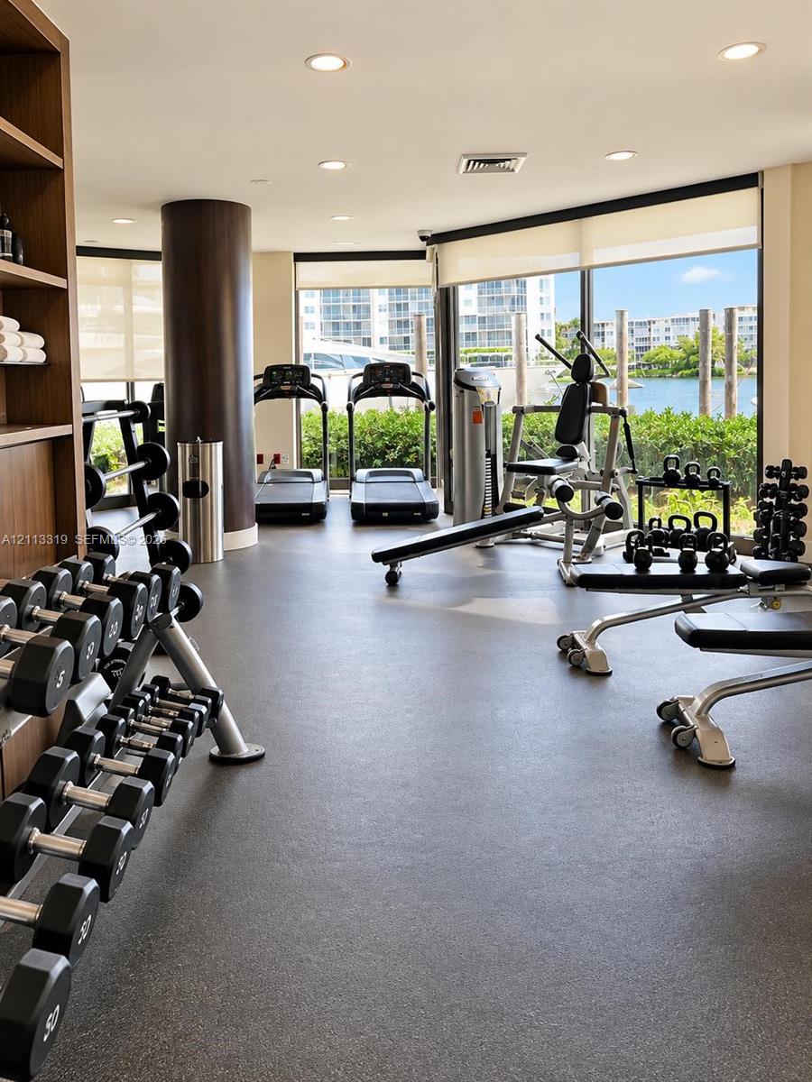 Fitness center featuring expansive floor-to-ceiling windows, rubberized athletic flooring, recessed lighting, and built-in shelving