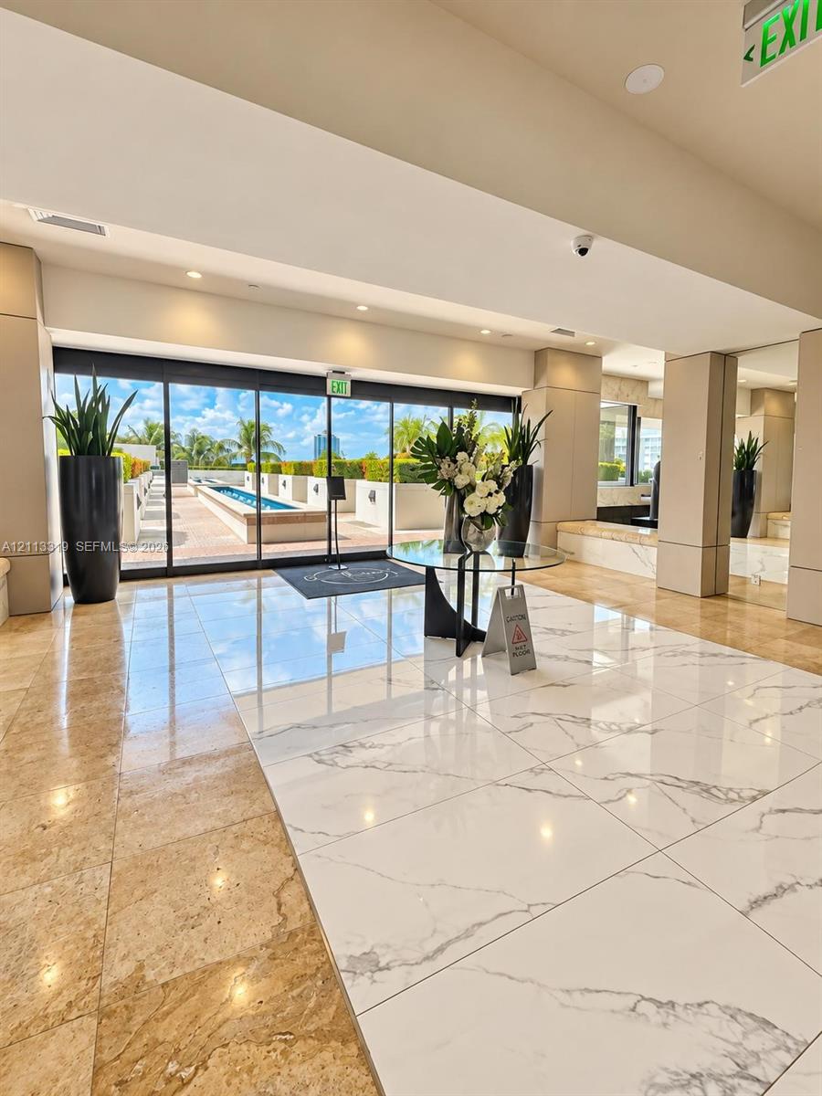 Lobby area featuring large-format polished stone flooring, floor-to-ceiling glass sliding doors, and direct access to an outdoor terrace with a linear water feature