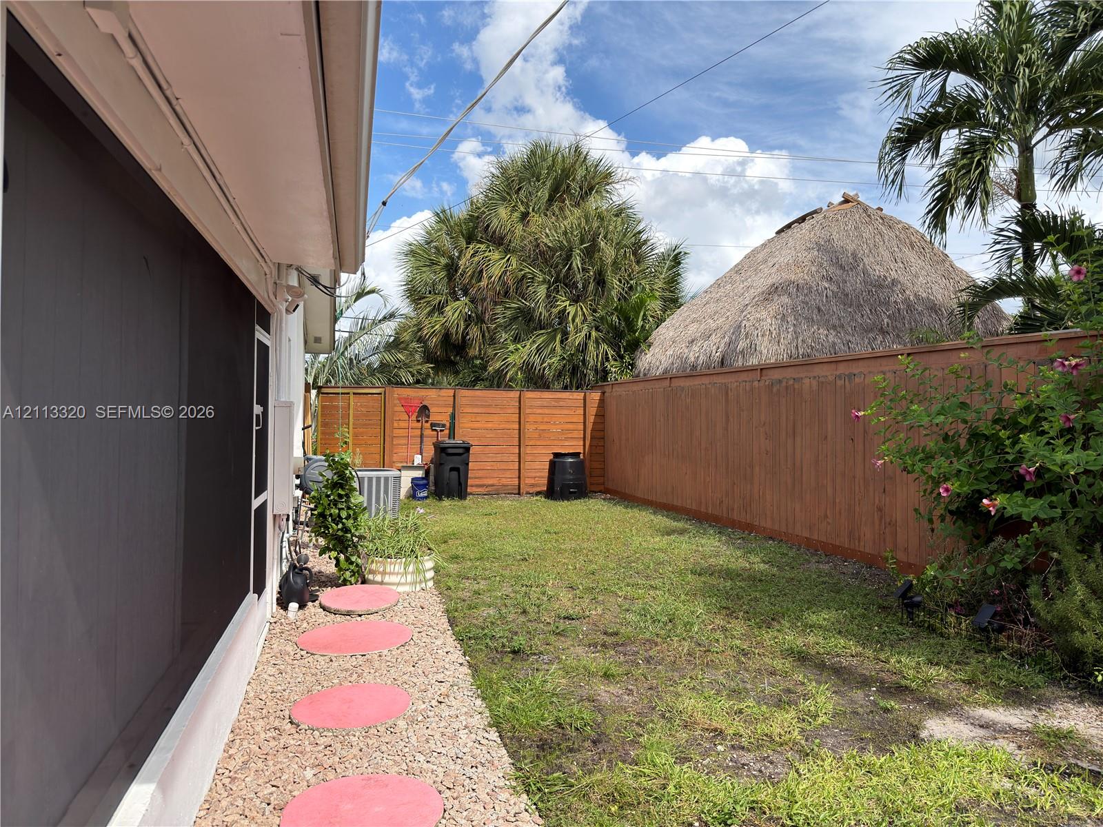 Private backyard featuring a horizontal wood-slat perimeter fence, gravel pathway with circular concrete pavers, and mature palm trees