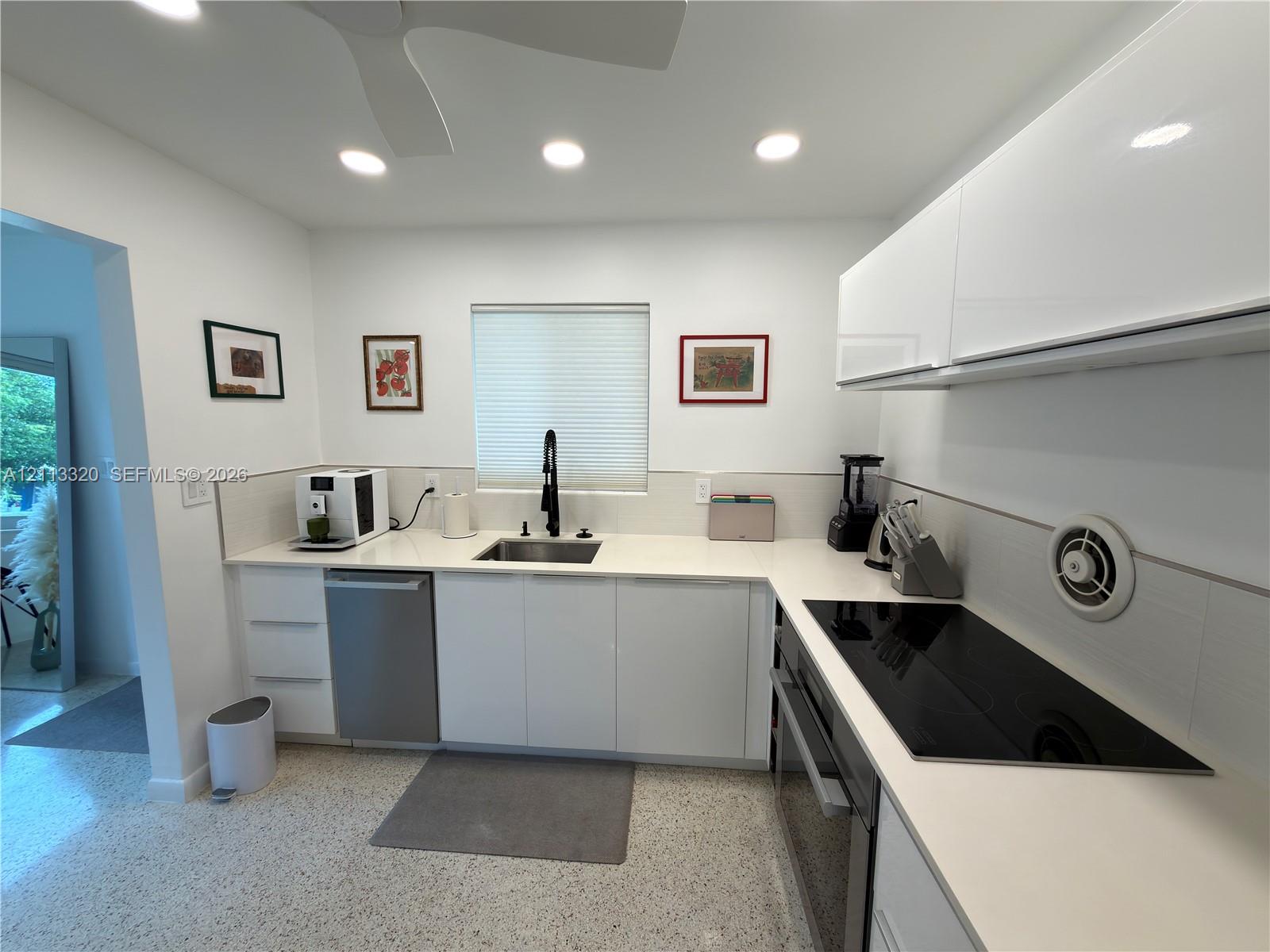 Kitchen featuring white high-gloss cabinetry, stone-finish countertops, stainless steel undermount sink with matte black gooseneck faucet, glass cooktop, and polished aggregate flooring