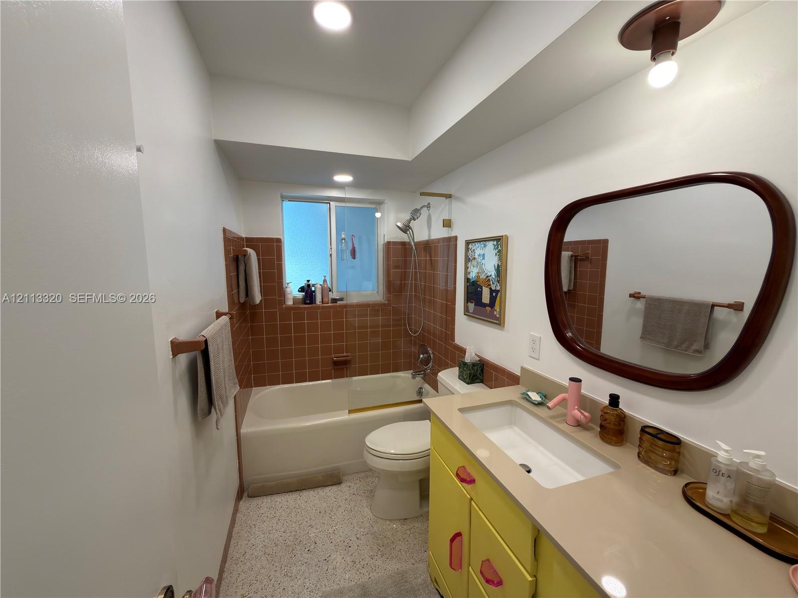 Bathroom featuring a vanity with integrated rectangular sink, solid surface countertop, tiled tub surround, recessed lighting, and terrazzo-style flooring