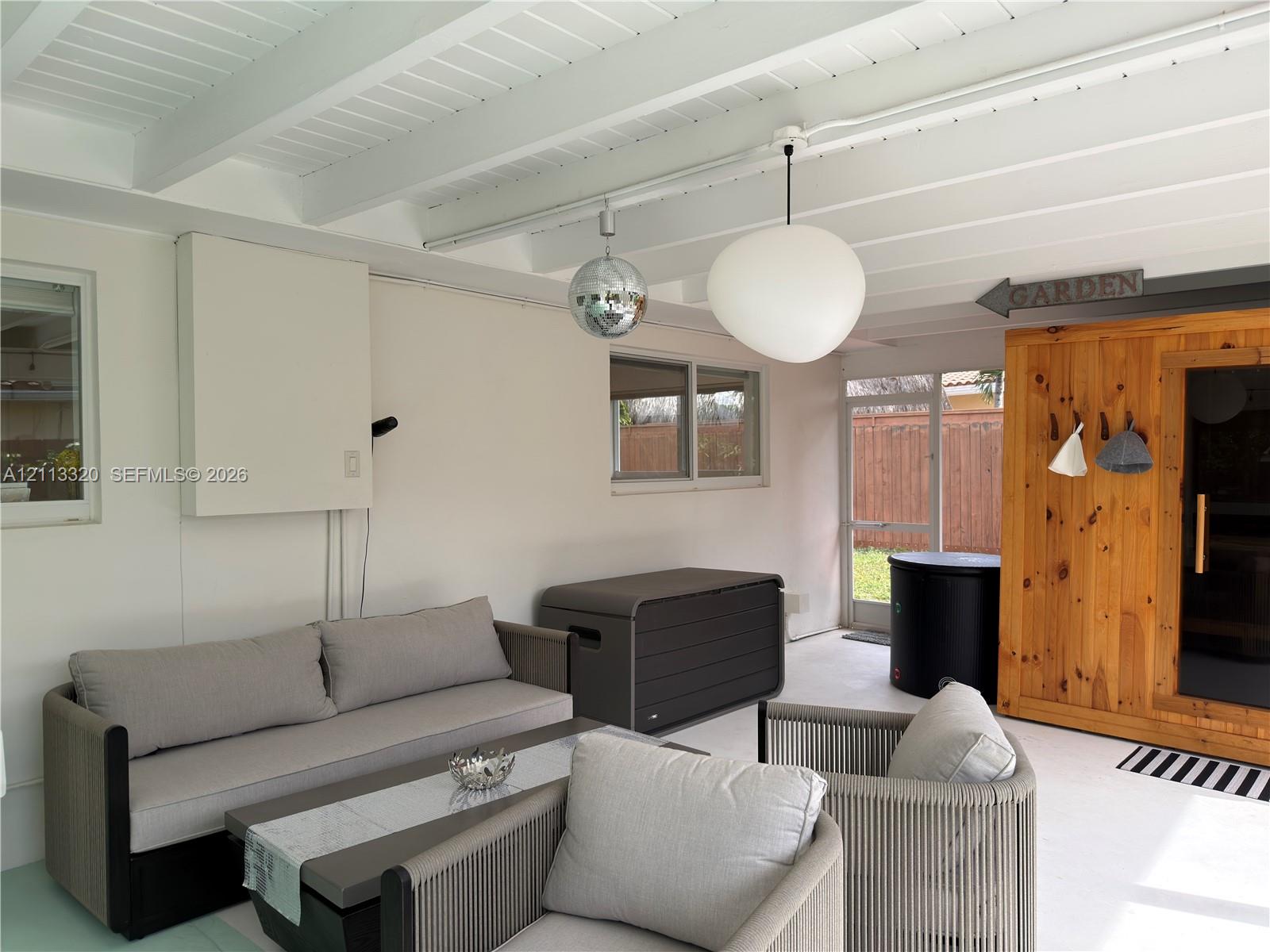 Covered patio featuring an exposed-beam ceiling, glass-paneled exterior door, pendant lighting, and a built-in wooden structure