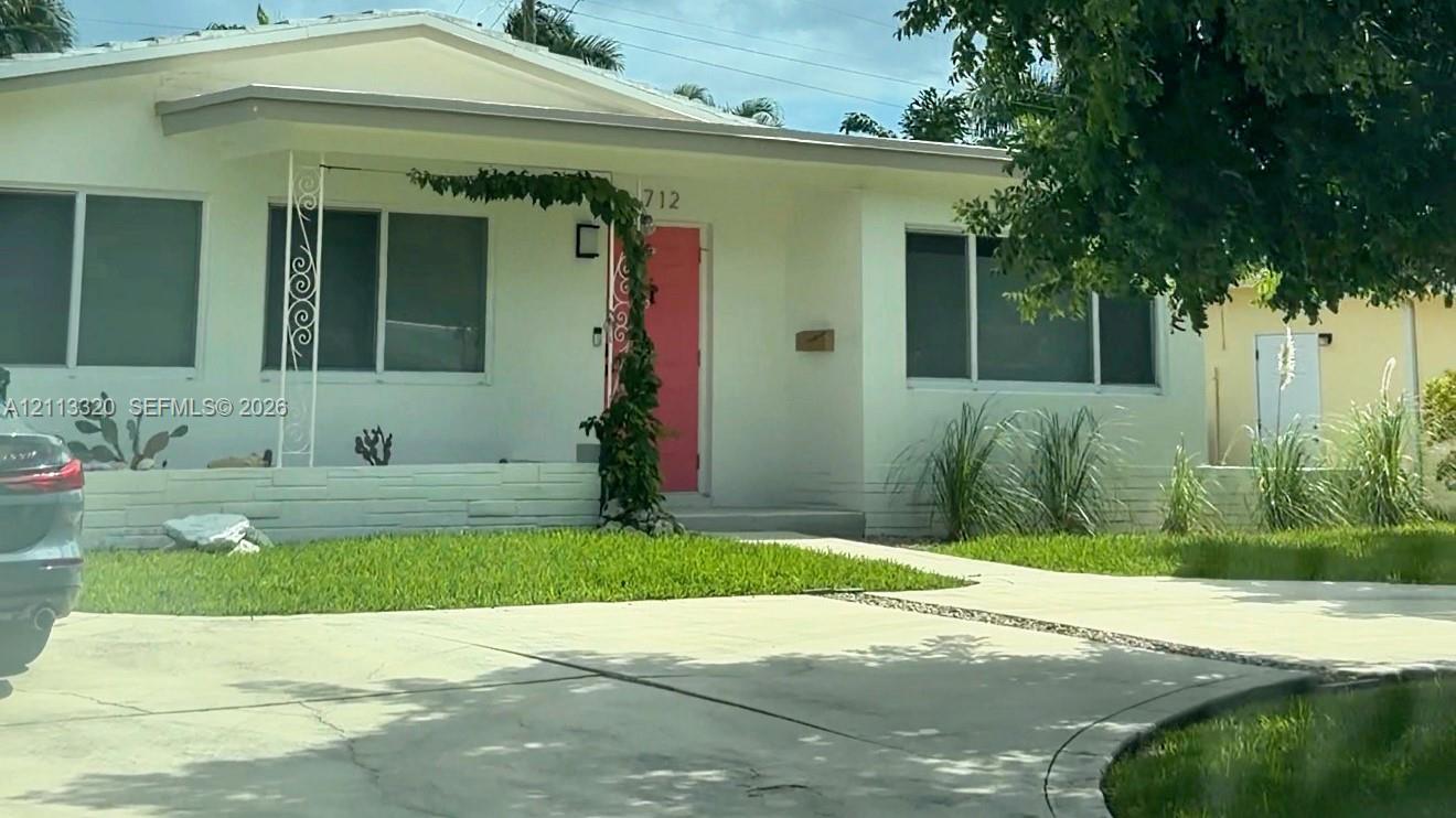 Single-story exterior featuring a light-colored stucco facade, decorative wrought iron porch support, a vibrant entry door, and a concrete driveway