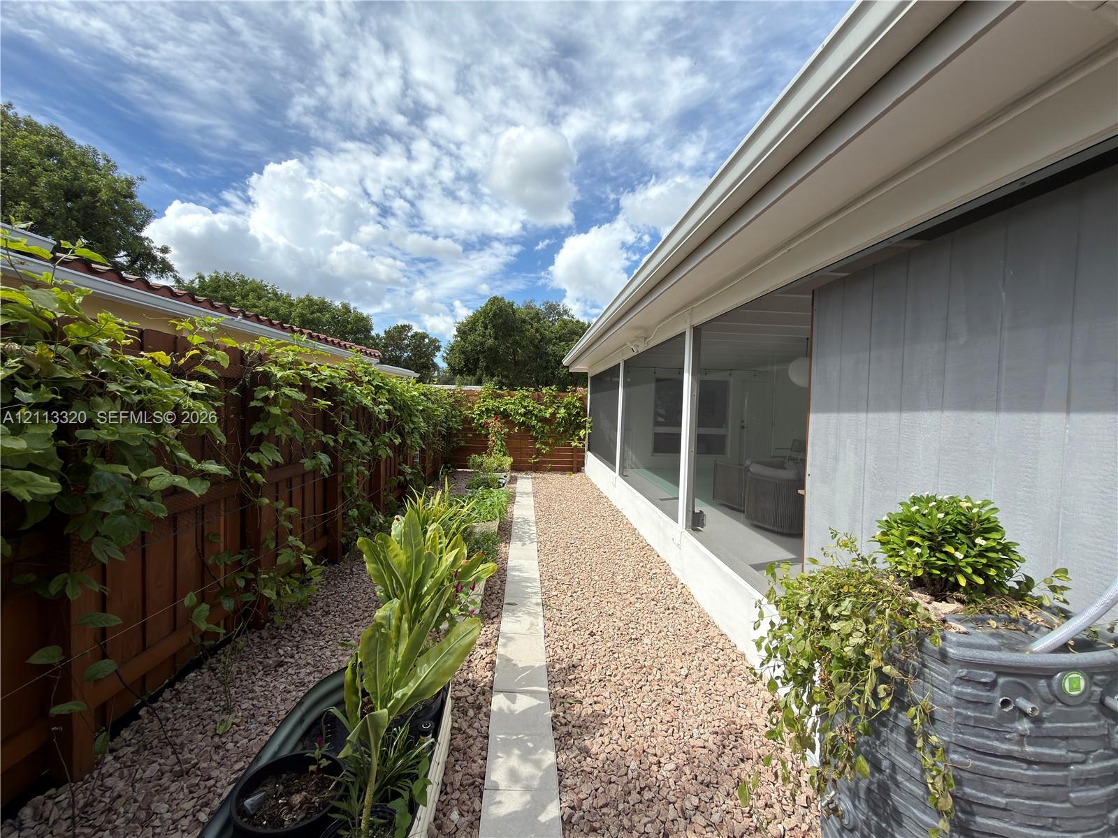Screened-in porch featuring a wood privacy fence, gravel ground cover, raised metal planter beds, and a built-in rainwater collection system