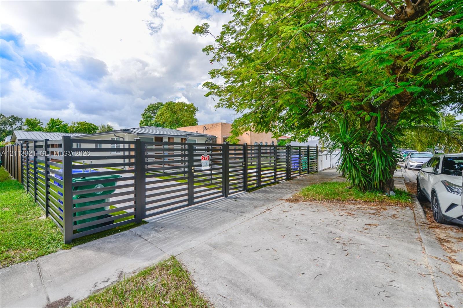 Horizontal slat metal perimeter fencing with integrated dual-swing entry gate and mature landscape canopy